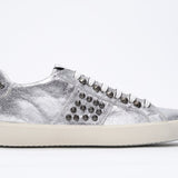 Side profile of low top metallic silver sneaker. Full leather upper with studs and vintage rubber sole.