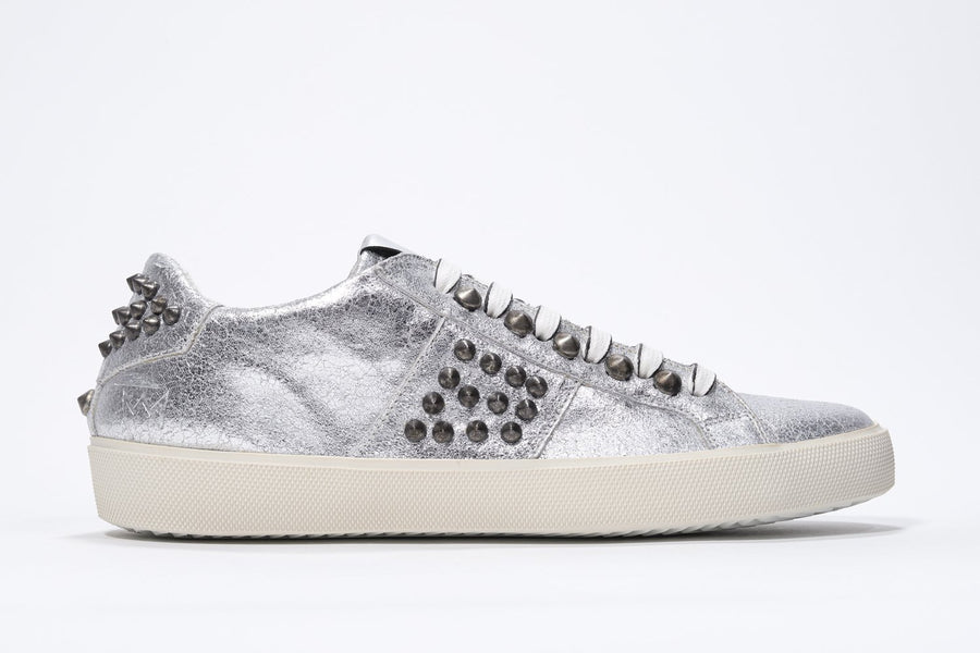 Side profile of low top metallic silver sneaker. Full leather upper with studs and vintage rubber sole.