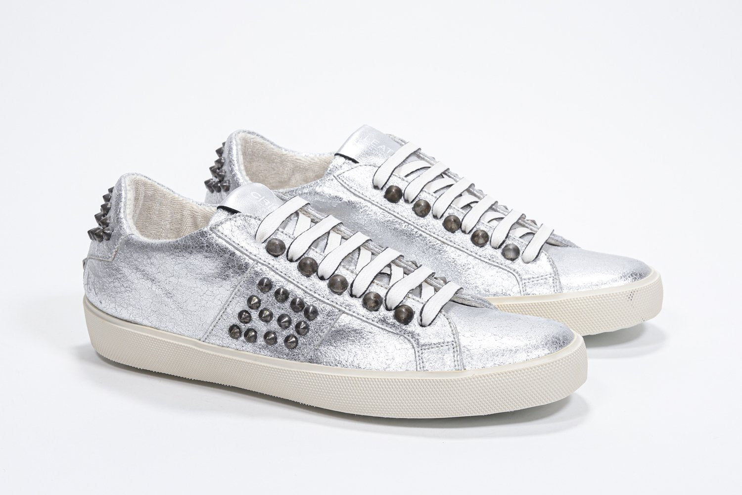 Three quarter front view of low top metallic silver sneaker. Full leather upper with studs and vintage rubber sole.