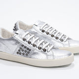Three quarter front view of low top metallic silver sneaker. Full leather upper with studs and vintage rubber sole.