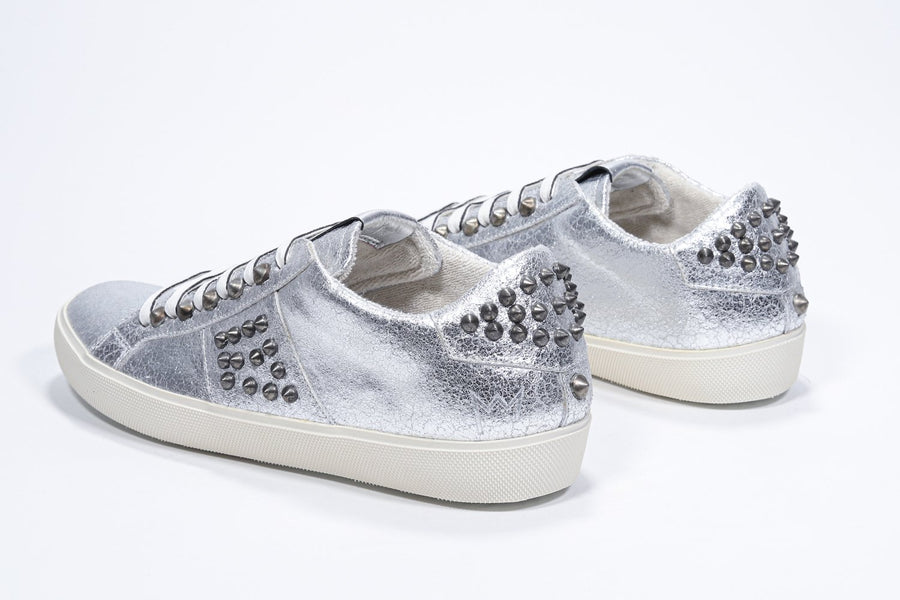 Three quarter back view of low top metallic silver sneaker. Full leather upper with studs and vintage rubber sole.