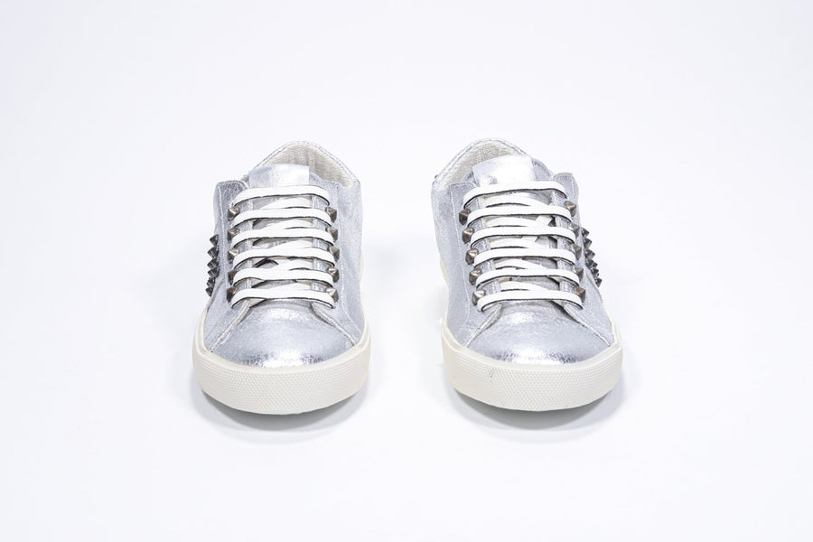 Front profile of low top metallic silver sneaker. Full leather upper with studs and vintage rubber sole.