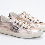 Three quarter front view of low top metallic rose sneaker. Full leather upper with studs and vintage rubber sole.