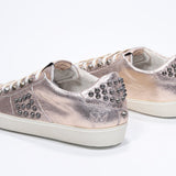Three quarter back view of low top metallic rose sneaker. Full leather upper with studs and vintage rubber sole.