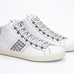 Three quarter front view of mid top white sneaker. Full leather upper with studs, an internal zip and vintage rubber sole.