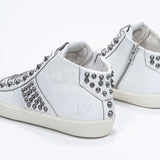 Three quarter back view of mid top white sneaker. Full leather upper with studs, an internal zip and vintage rubber sole.
