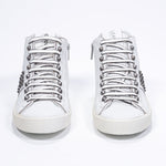 Front view of mid top white sneaker. Full leather upper with studs, an internal zip and vintage rubber sole.