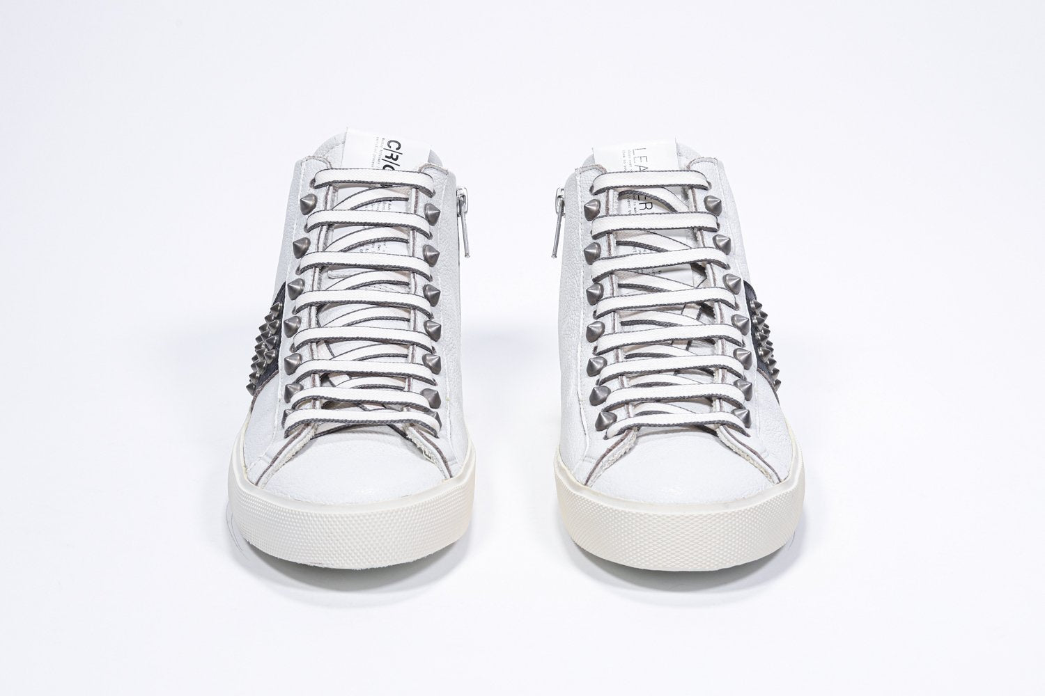 Front view of mid top white and black sneaker. Full leather upper with studs, an internal zip and vintage rubber sole.