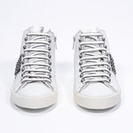 Vista frontale della mid top bianca e nera sneaker. Tomaia in pelle con borchie, zip interna e suola in gomma vintage.