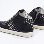 Three quarter back view of mid top black sneaker. Full leather upper with studs, an internal zip and vintage rubber sole.