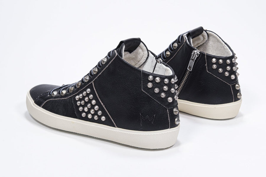 Three quarter back view of mid top black sneaker. Full leather upper with studs, an internal zip and vintage rubber sole.