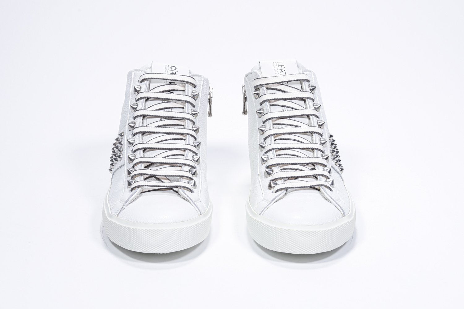 Vista frontale del mid top bianco sneaker. Tomaia in pelle con borchie, zip interna e suola in gomma bianca.