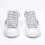 Vista frontale del mid top bianco sneaker. Tomaia in pelle con borchie, zip interna e suola in gomma bianca.