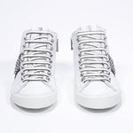 Vue de face d'une paire de chaussures blanches et noires sneaker. Tige en cuir avec clous, fermeture à glissière interne et semelle en caoutchouc blanc.