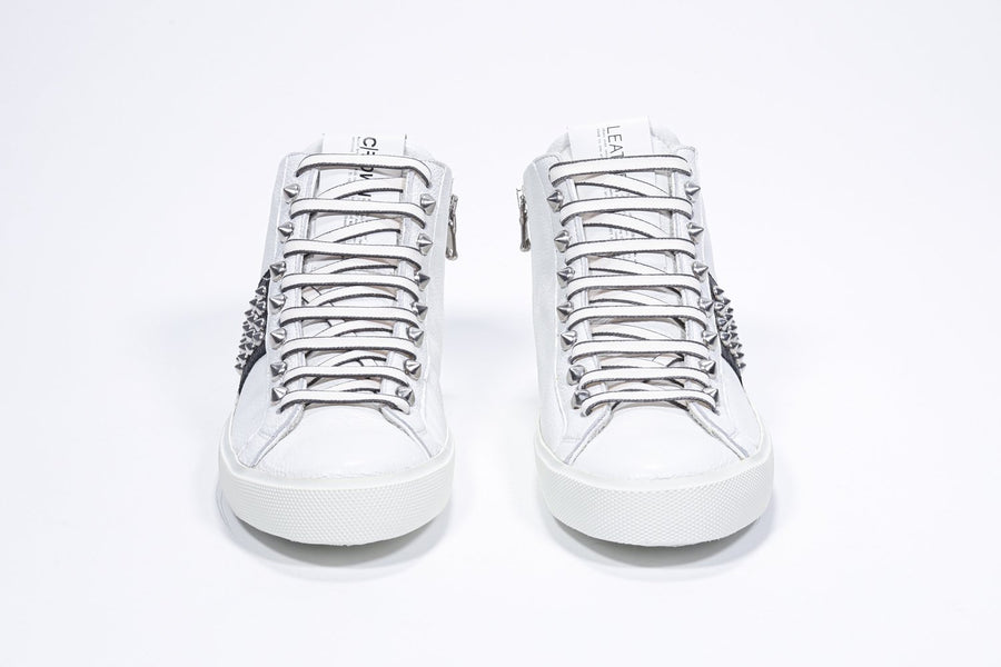 Front view of mid top white and black sneaker. Full leather upper with studs, an internal zip and white rubber sole.