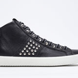 Profilo laterale del mid top nero sneaker. Tomaia in pelle con borchie, zip interna e suola in gomma bianca.