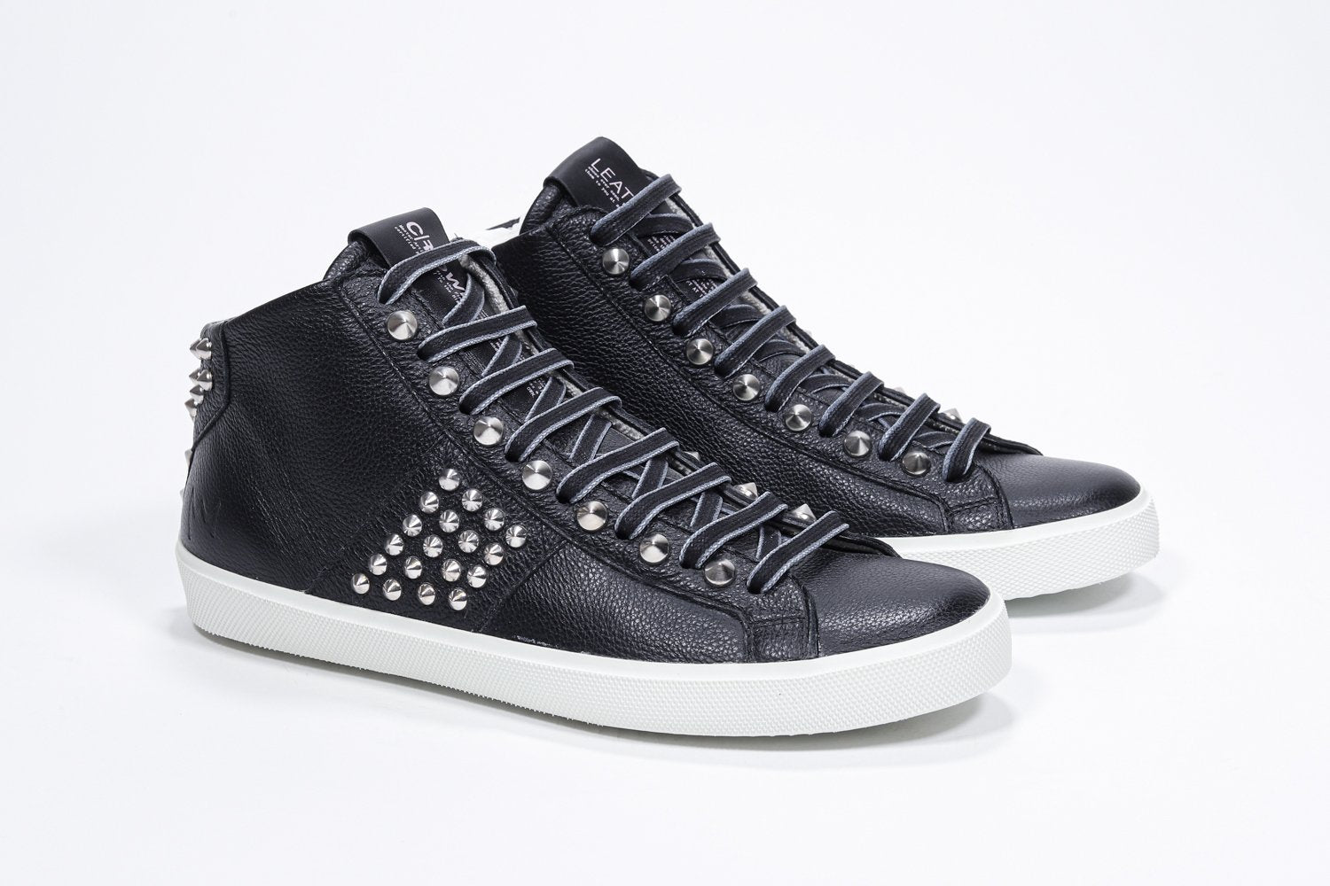 Three quarter front view of mid top black sneaker. Full leather upper with studs, an internal zip and white rubber sole.