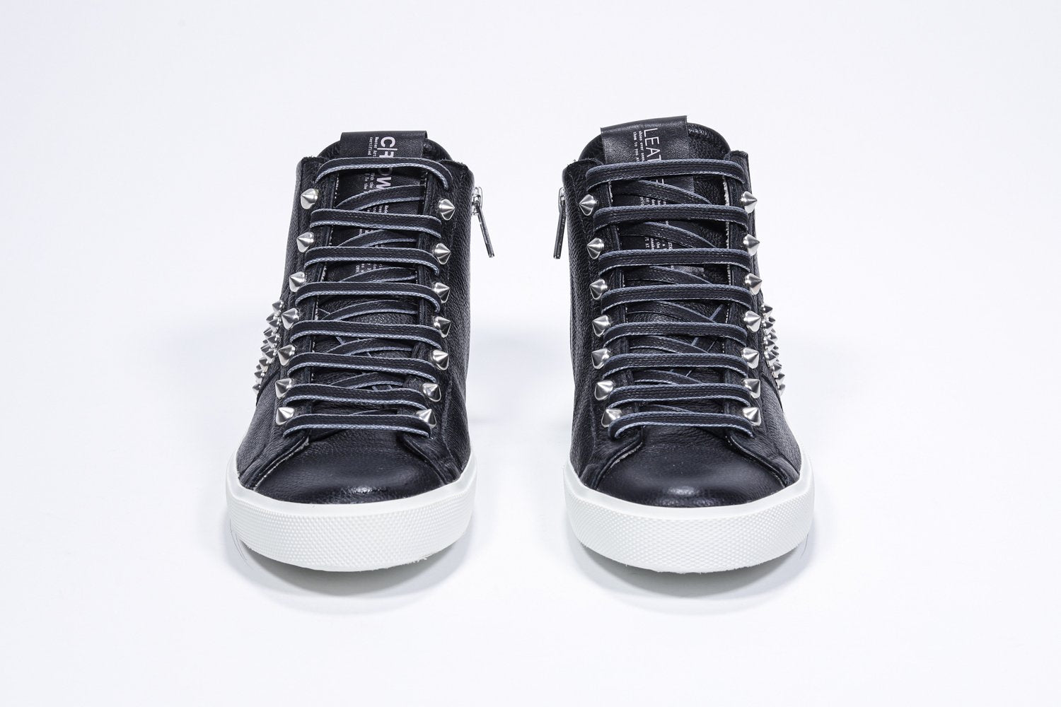 Vista frontale del mid top nero sneaker. Tomaia in pelle con borchie, zip interna e suola in gomma bianca.