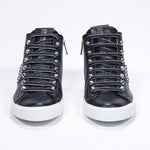 Front view of mid top black sneaker. Full leather upper with studs, an internal zip and white rubber sole.