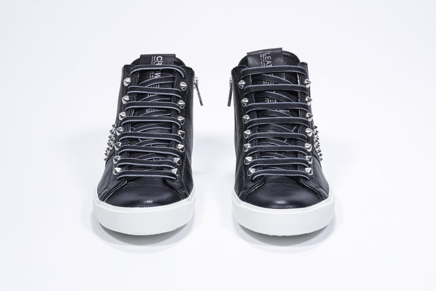 Front view of mid top black sneaker. Full leather upper with studs, an internal zip and white rubber sole.