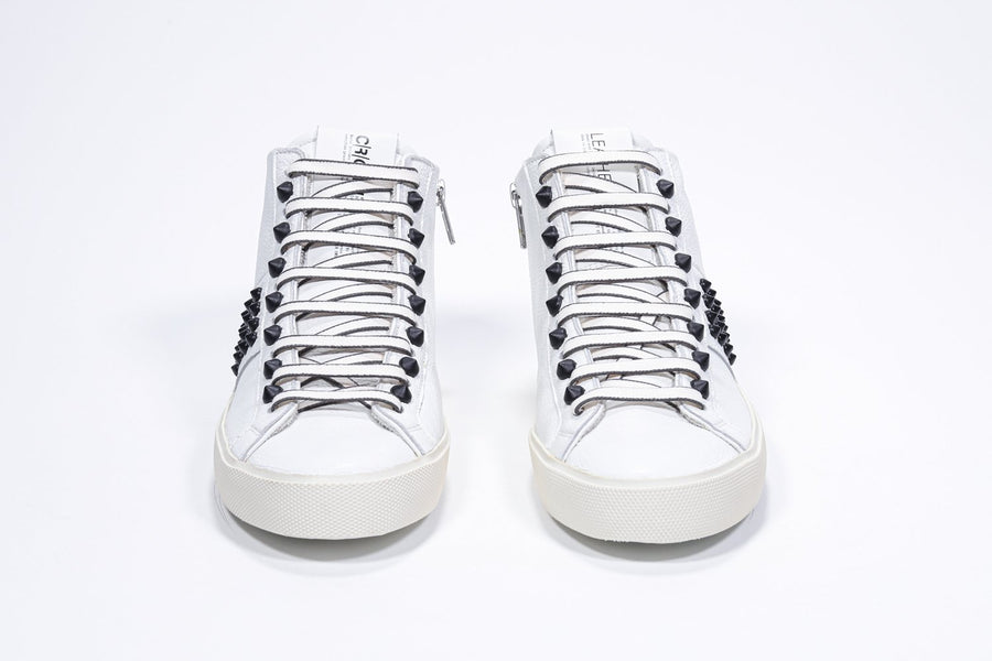 Front view of mid top white sneaker. Full leather upper with studs, an internal zip and vintage rubber sole.