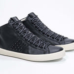 Three quarter front view of mid top black sneaker. Full leather upper with studs, an internal zip and vintage rubber sole.