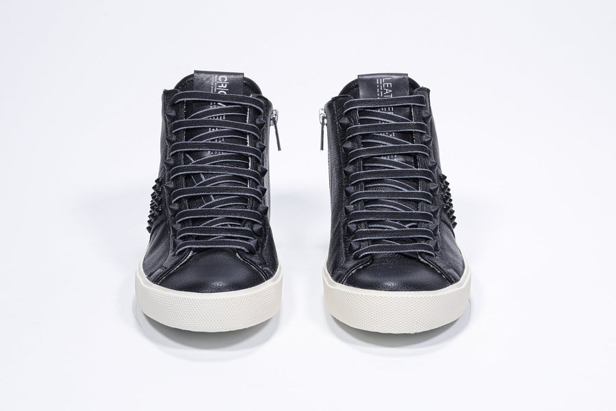 Front view of mid top black sneaker. Full leather upper with studs, an internal zip and vintage rubber sole.