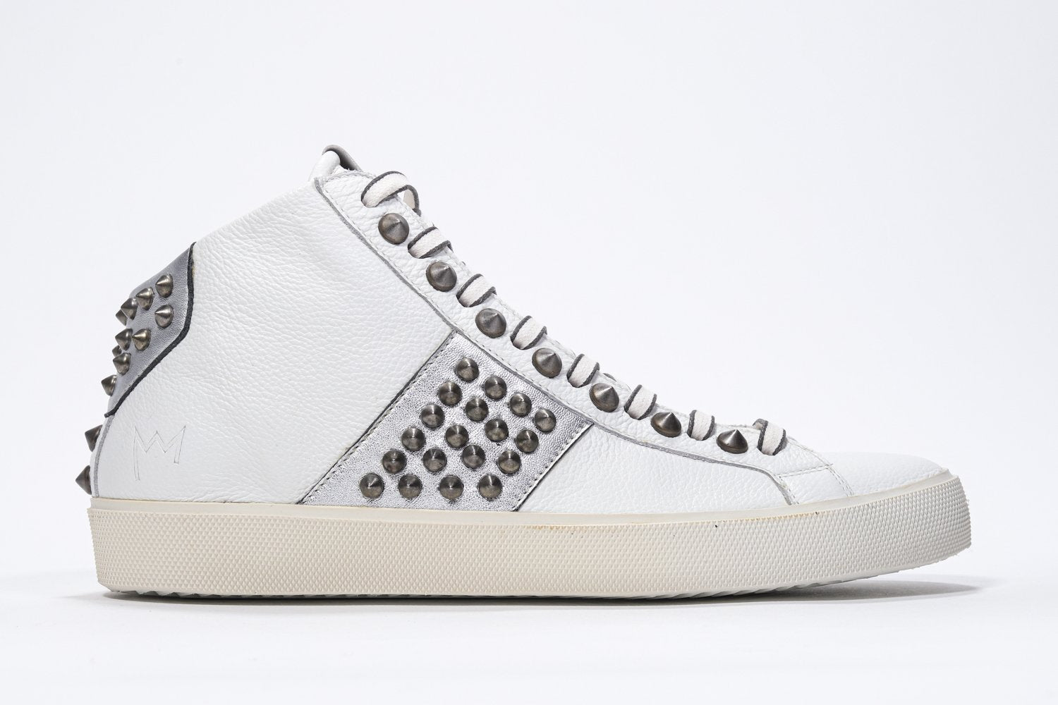 Side profile of mid top white and metallic silver sneaker. Full leather upper with studs, an internal zip and vintage rubber sole.