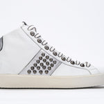 Side profile of mid top white and metallic silver sneaker. Full leather upper with studs, an internal zip and vintage rubber sole.