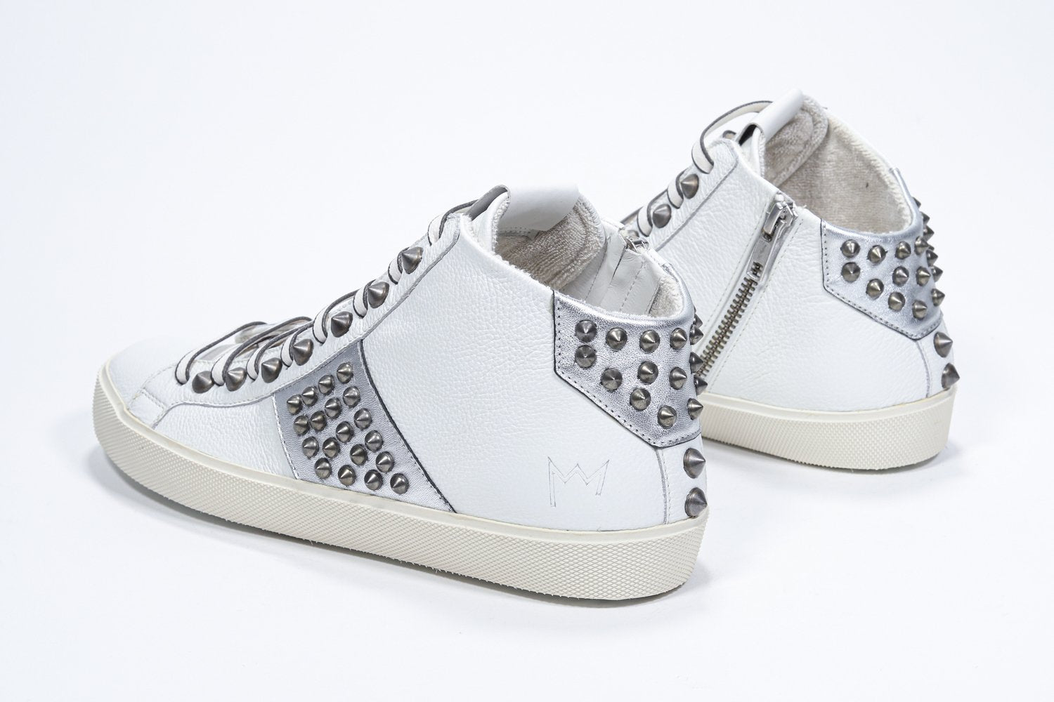 Three quarter back view of mid top white and metallic silver sneaker. Full leather upper with studs, an internal zip and vintage rubber sole.