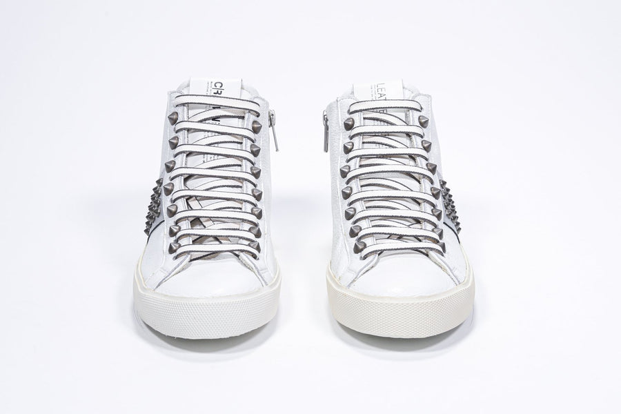Front view of mid top white and metallic silver sneaker. Full leather upper with studs, an internal zip and vintage rubber sole.