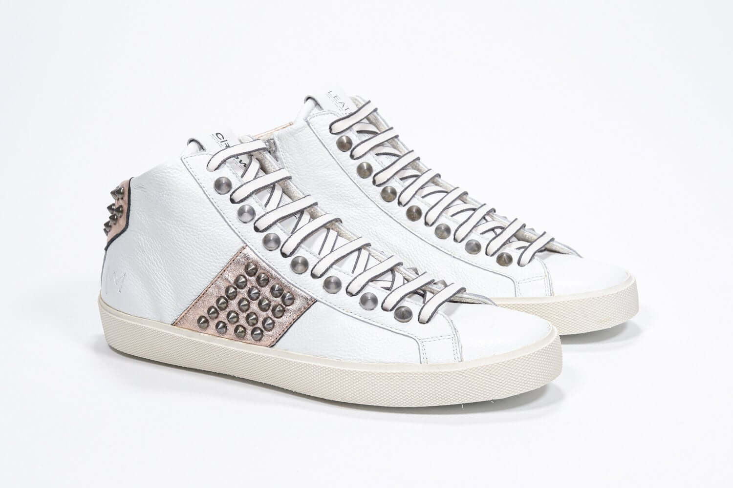 Three quarter front view of mid top white and metallic rose sneaker. Full leather upper with studs, an internal zip and vintage rubber sole.