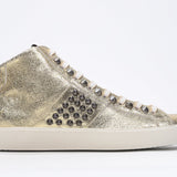 Side profile of mid top metallic gold sneaker. Full leather upper with studs, an internal zip and vintage rubber sole.