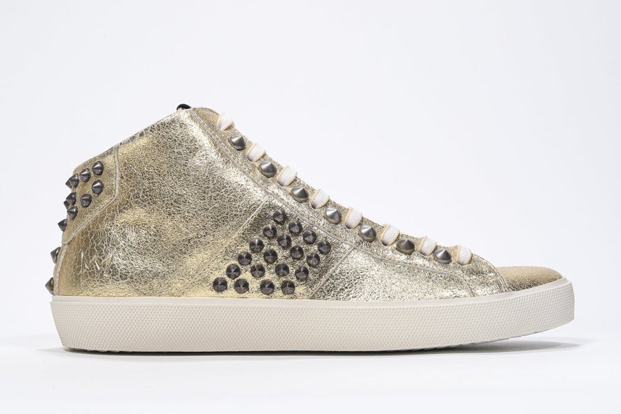 Side profile of mid top metallic gold sneaker. Full leather upper with studs, an internal zip and vintage rubber sole.