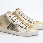 Three quarter front view of mid top metallic gold sneaker. Full leather upper with studs, an internal zip and vintage rubber sole.
