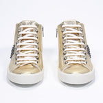 Front view of mid top metallic gold sneaker. Full leather upper with studs, an internal zip and vintage rubber sole.