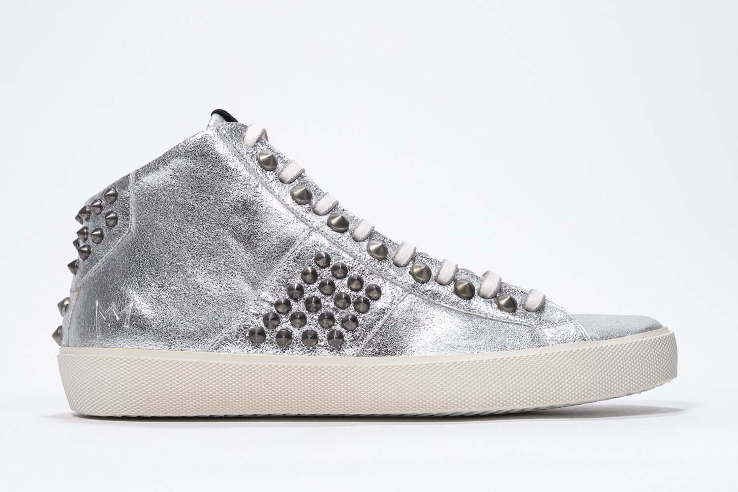 Side profile of mid top metallic silver sneaker. Full leather upper with studs, an internal zip and vintage rubber sole.