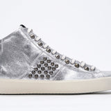 Side profile of mid top metallic silver sneaker. Full leather upper with studs, an internal zip and vintage rubber sole.