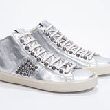 Three quarter front view of mid top metallic silver sneaker. Full leather upper with studs, an internal zip and vintage rubber sole.