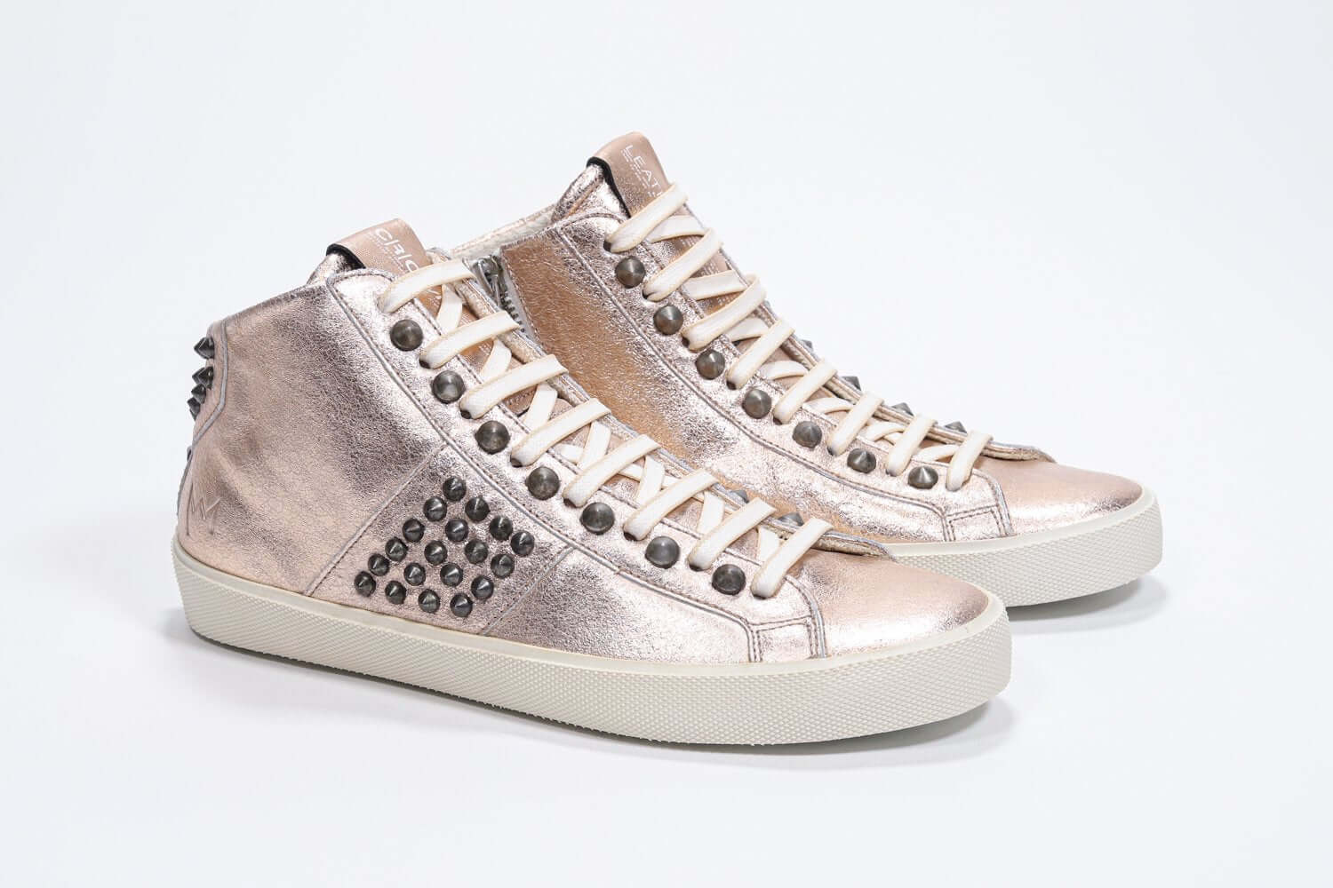 Vue de trois quarts avant d'un modèle intermédiaire en rose métallique sneaker. Tige en cuir avec clous, fermeture éclair intérieure et semelle en caoutchouc vintage.