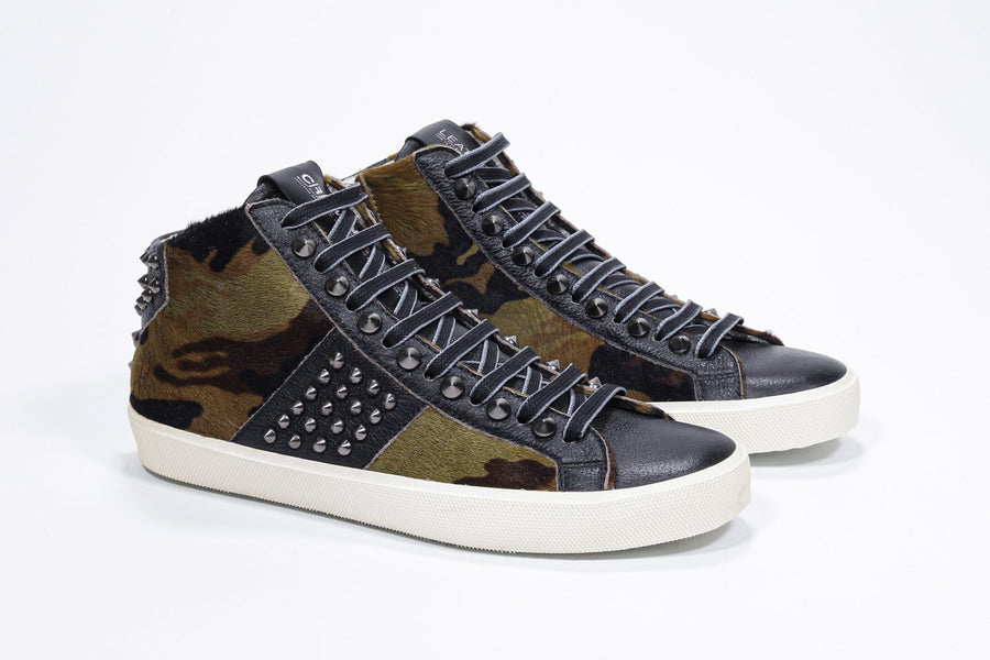 Three quarter front view of mid top camouflage print sneaker. Haircalf and leather upper with studs, an internal zip and vintage rubber sole.