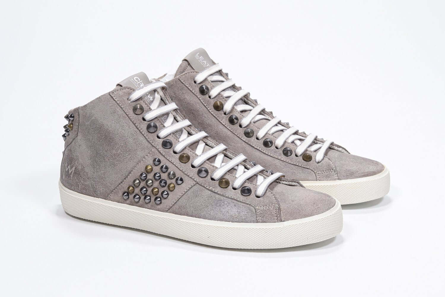 Vue de trois quarts de l'avant de la chaussure de couleur beige sneaker. Tige en daim avec clous, fermeture à glissière intérieure et semelle en caoutchouc vintage.