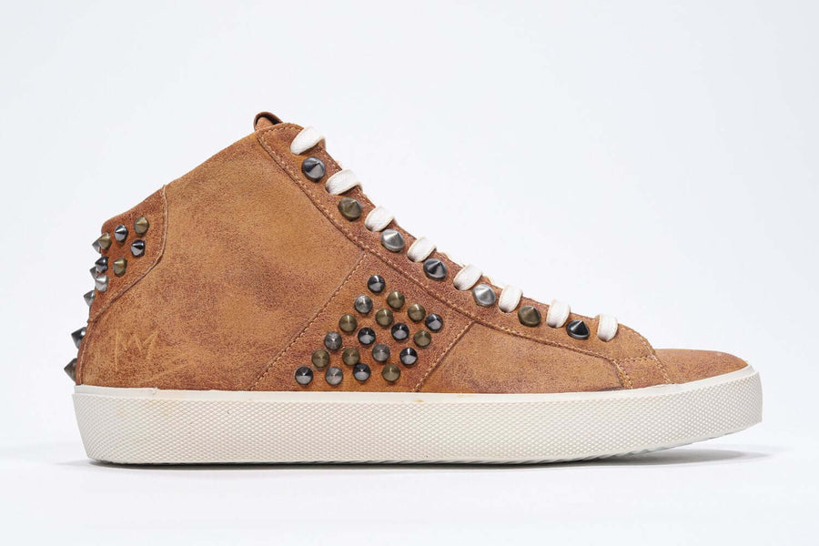 Side profile of mid top rust color sneaker. Full suede upper with studs, an internal zip and vintage rubber sole.