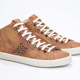 Three quarter front view of mid top rust color sneaker. Full suede upper with studs, an internal zip and vintage rubber sole.