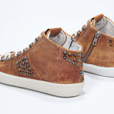 Three quarter back view of mid top rust color sneaker. Full suede upper with studs, an internal zip and vintage rubber sole.