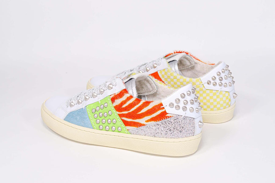 Three quarter back view of low top sneaker. Patchwork upper of mixed materials and silver studs.