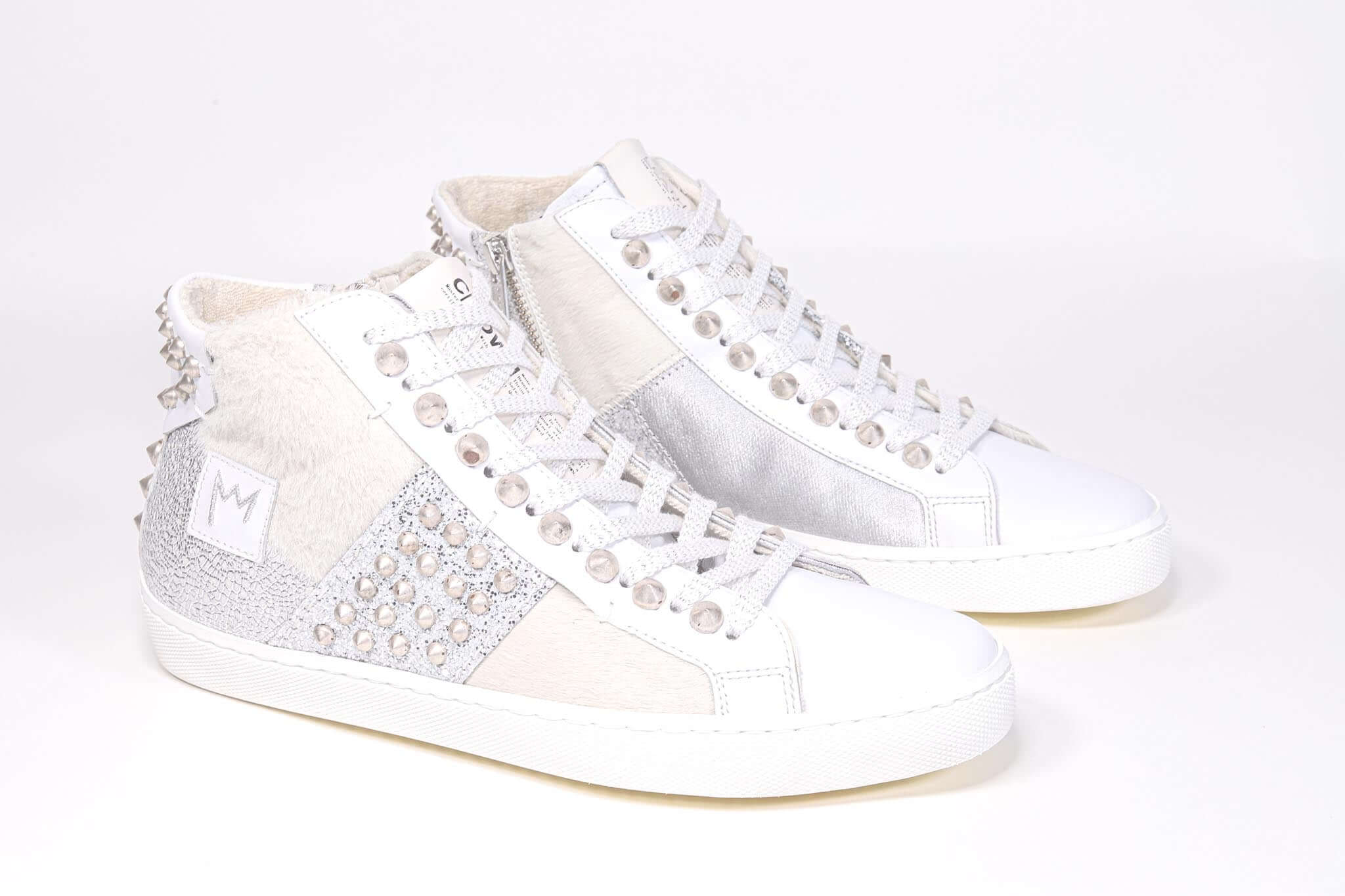 Three quarter front view of mid top sneaker. Patchwork upper of mixed materials and silver studs.