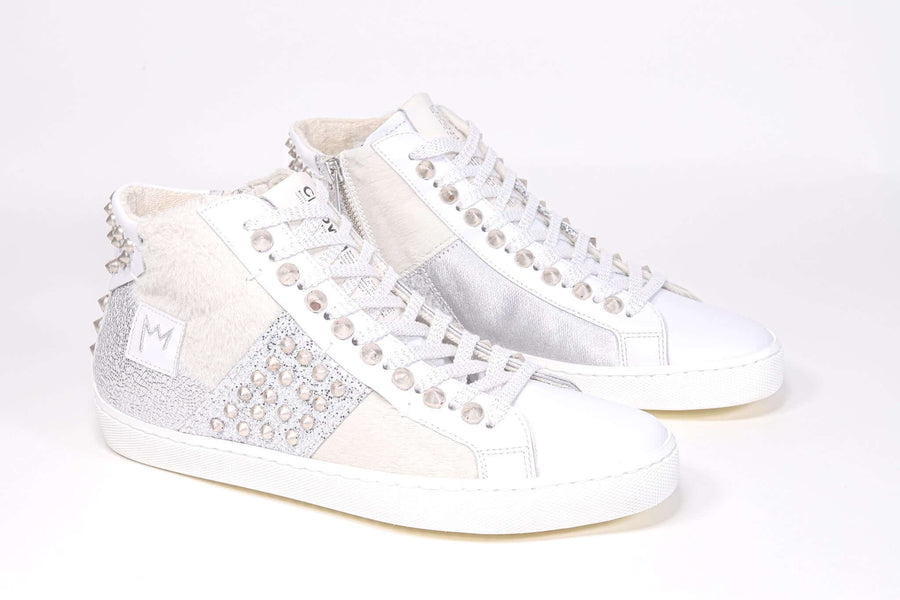 Three quarter front view of mid top sneaker. Patchwork upper of mixed materials and silver studs.