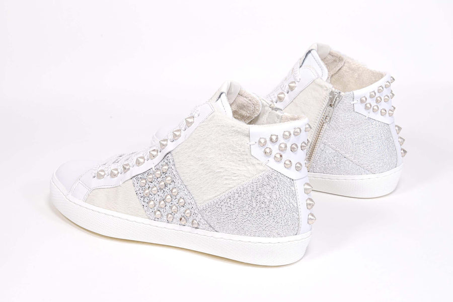 Three quarter back view of mid top sneaker. Patchwork upper of mixed materials and silver studs.