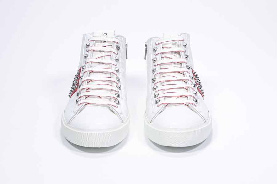 Vorderansicht des weißen und roten Mid-Top-Sneakers. Obermaterial aus Vollleder mit Nieten, einem internen Reißverschluss und weißer Gummisohle.